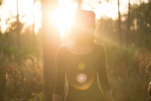 一名女性在樹林間，背對強烈的陽光的照片。